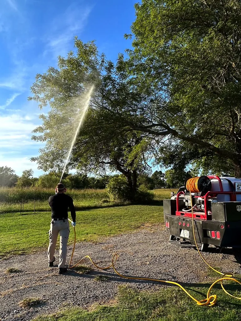 Bret Elza spraying trees for perimeter pest control at a wooded property